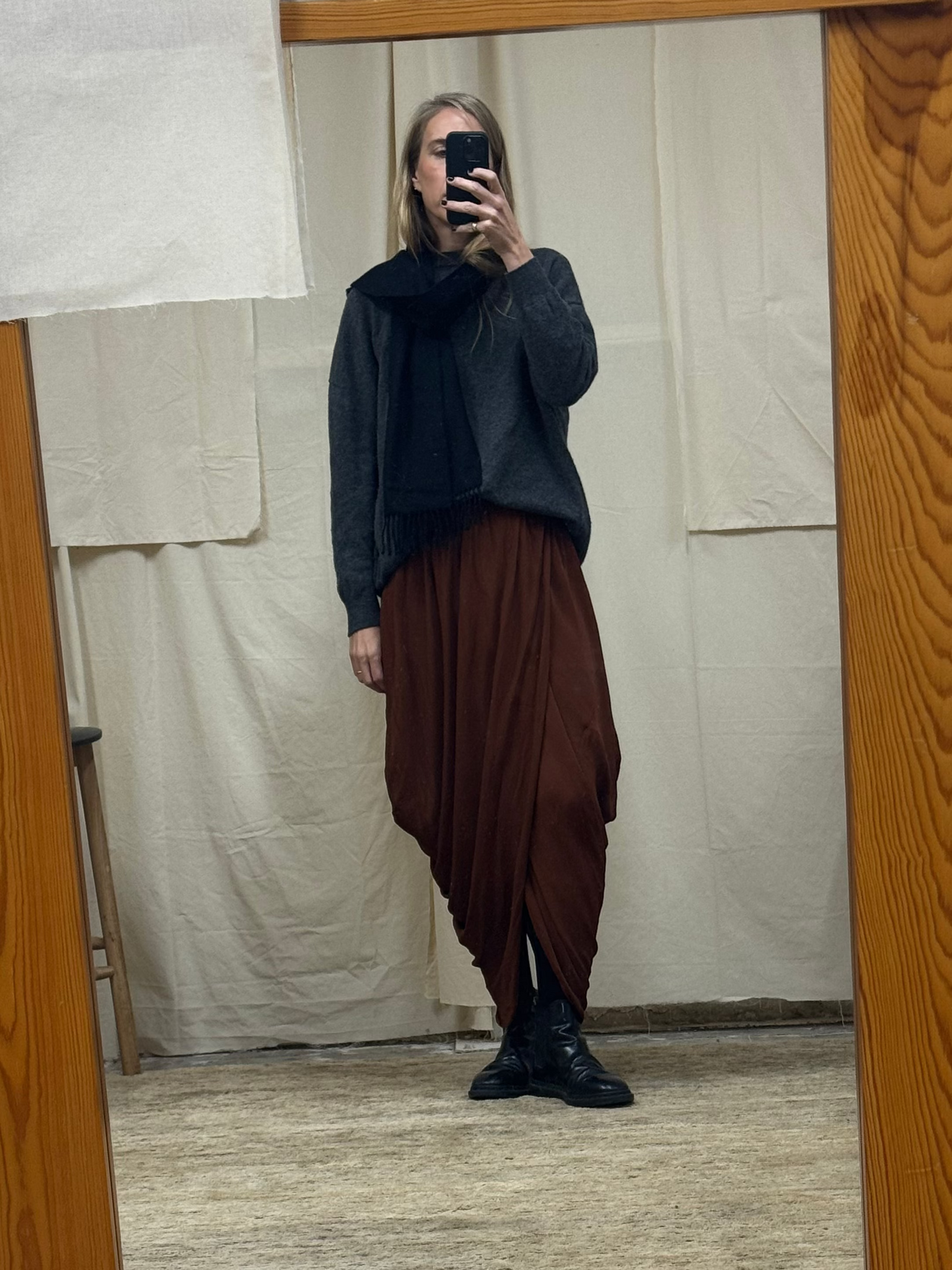 Person taking a mirror selfie wearing a dark sweater and brown pants in front of a wooden-framed mirror.