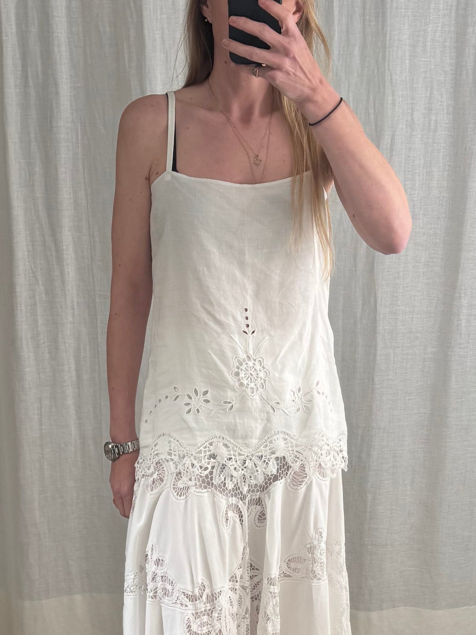 Woman wearing a white lace dress in a room with a mirror.